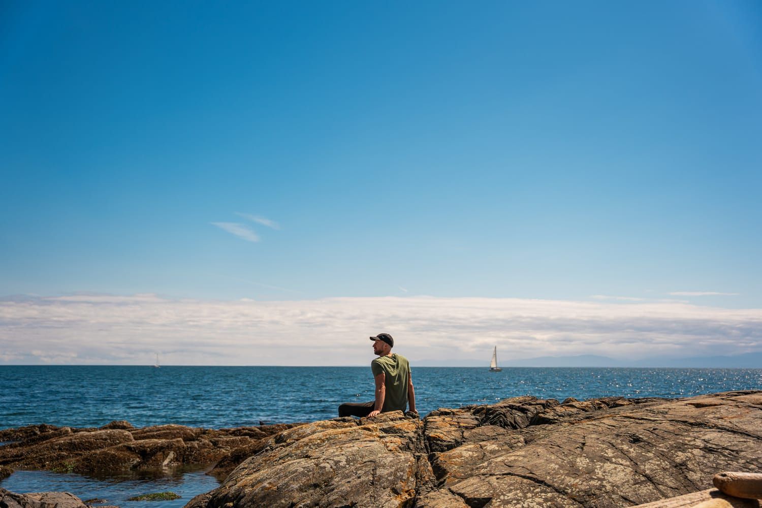 Andras Lenart sitting on rocks at the ocean's edge near Victoria, BC, looking out to sea